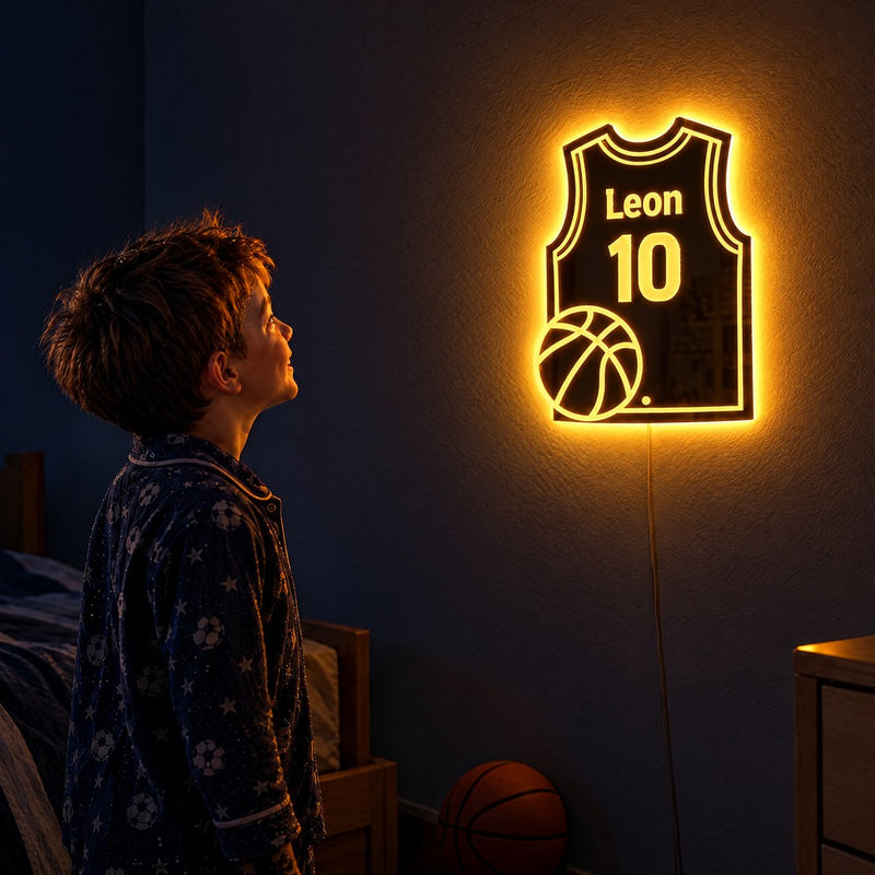 Un garçon en pyjama contemple, émerveillé, son miroir maillot de basket à la lueur chaude, avec son prénom et son numéro